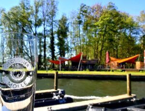 Glas mit der Beschriftung "Blossiner Molle" am Wasser mit Blick auf das Hafencafe namens Palstek.