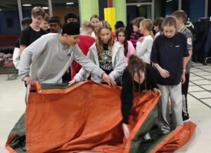 Eine Gruppe Jugendlicher steht gemeinsam auf einer Plane und macht eine Teamübung.